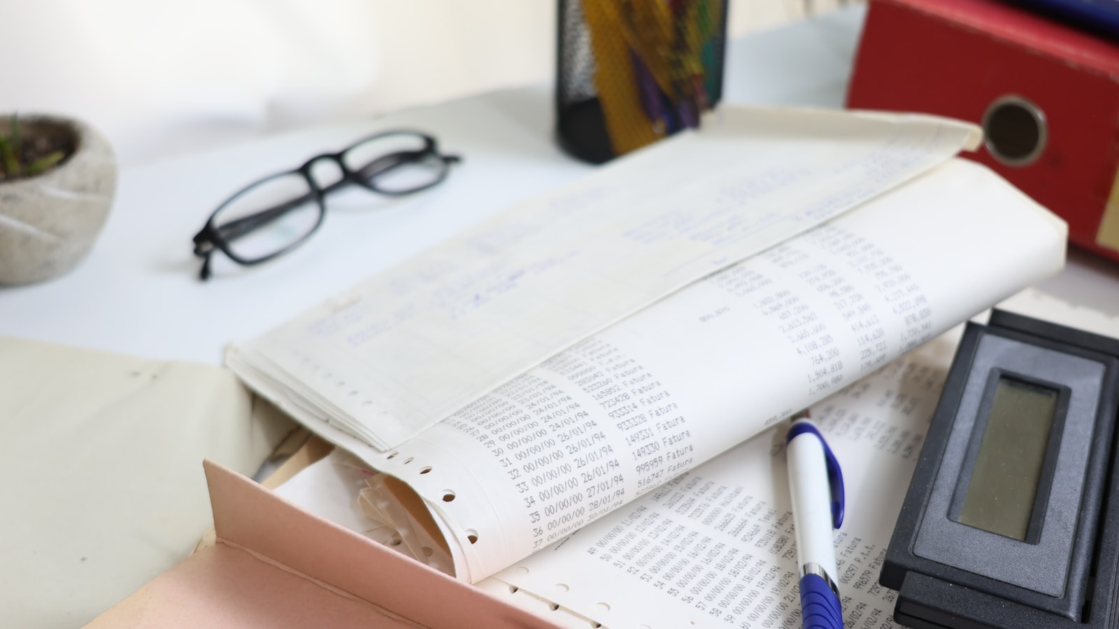 Mesa com calculadora, papéis e óculos representando o cálculo do custo de um sistema de gestão escolar